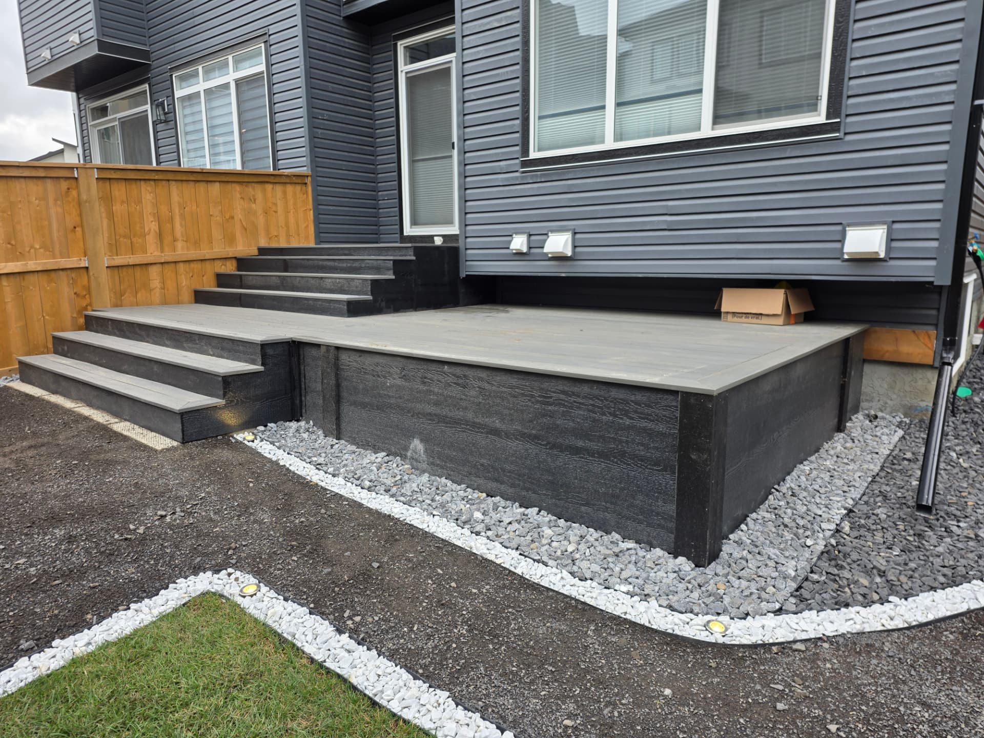 Charcoal composite deck with wide steps and cedar fence built in a Calgary backyard