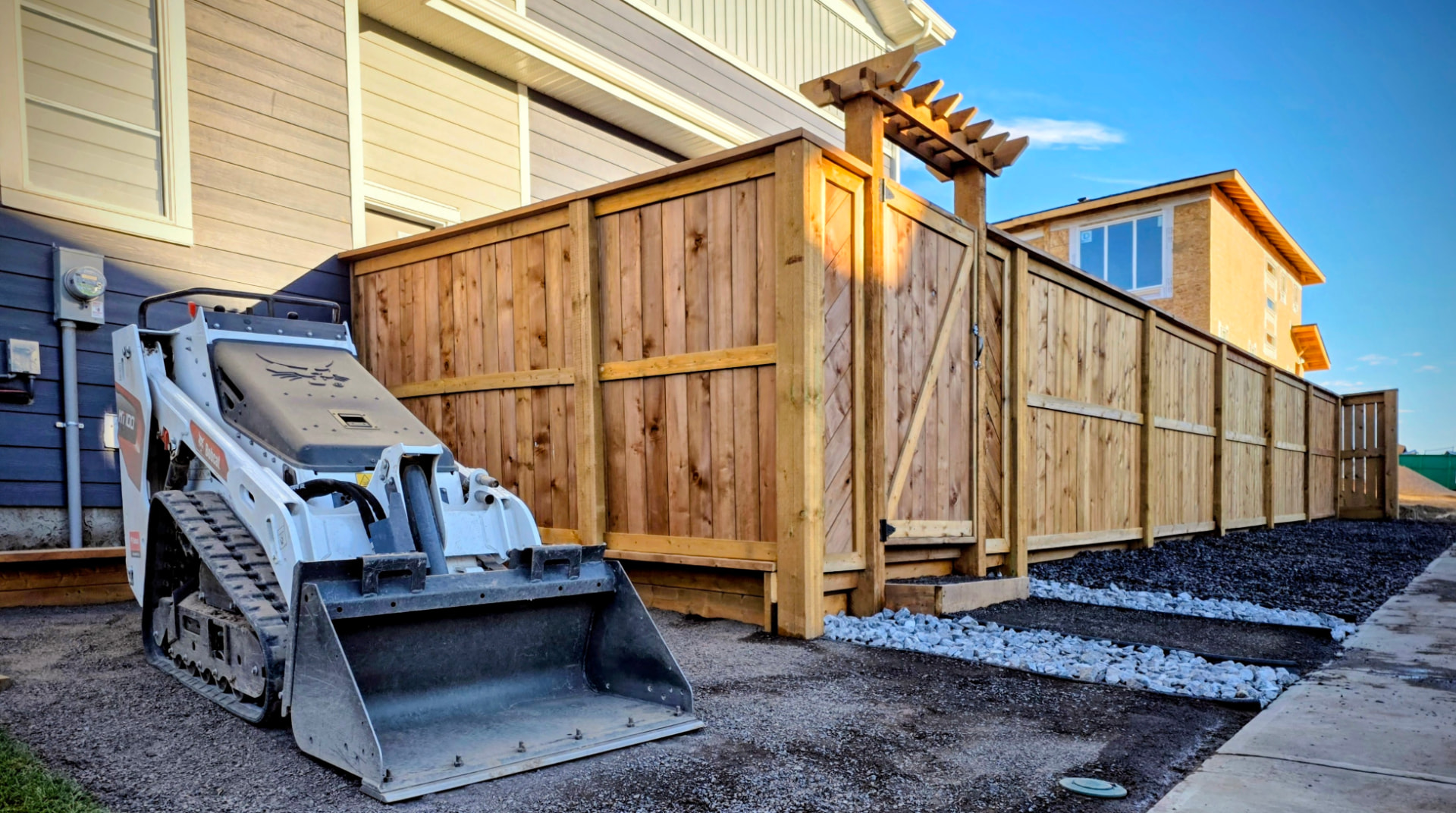 New cedar fence with pergola-topped gate and gravel edging