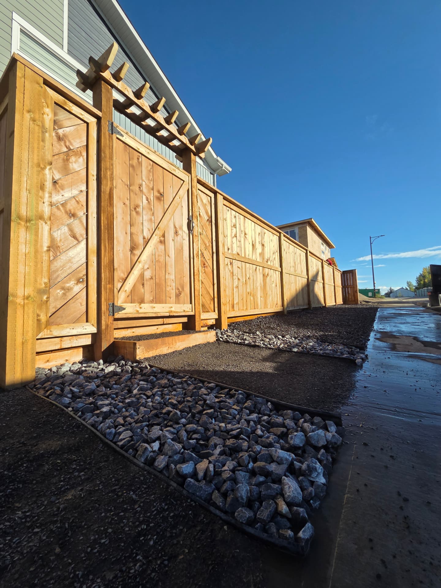 Cedar fence with pergola-topped gate and rock drainage bed in evening sun