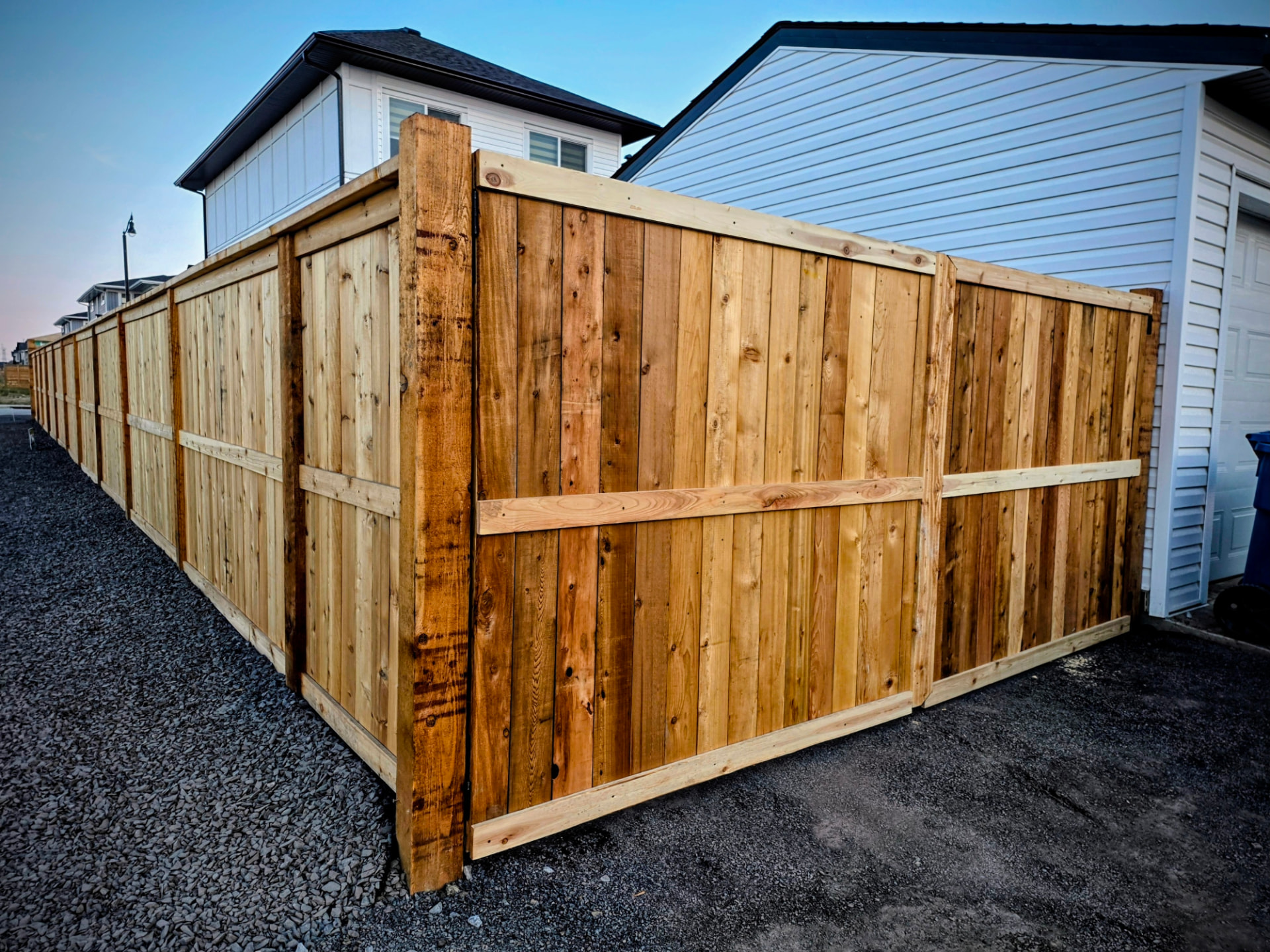 Tall cedar privacy fence corner beside a garage at dusk